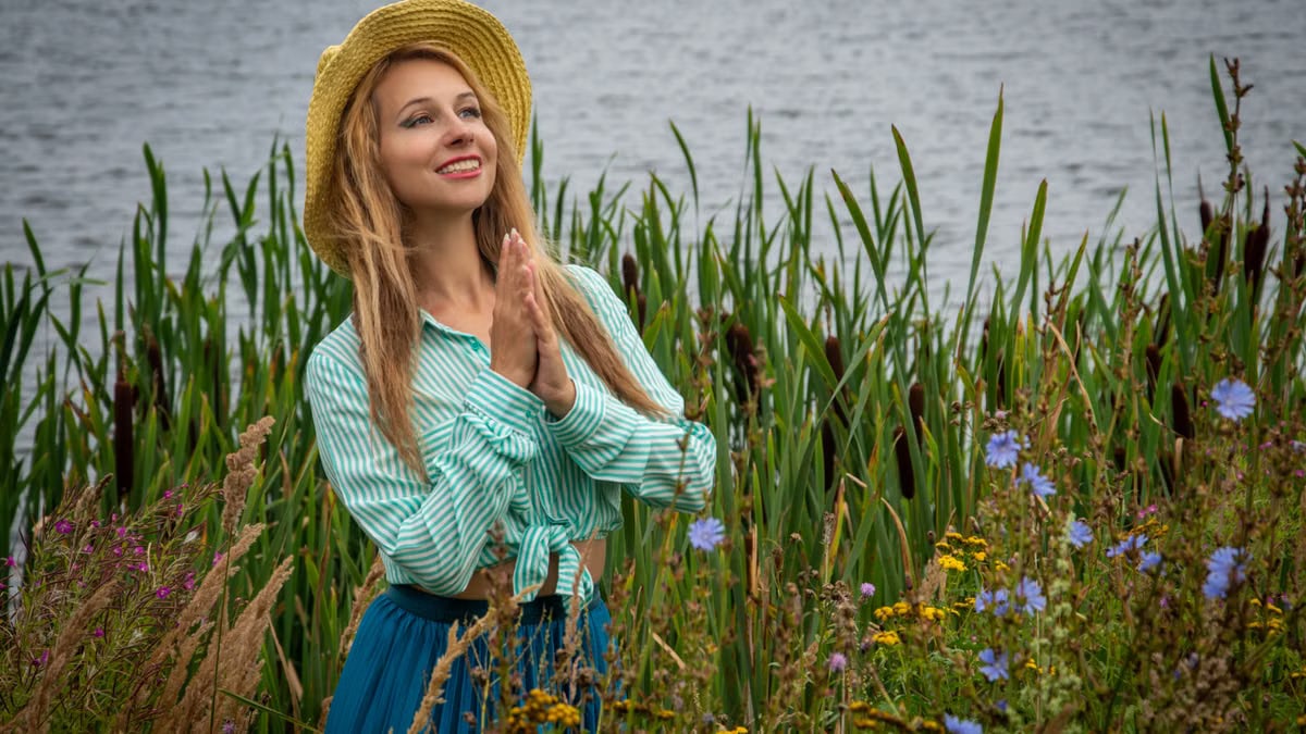 Smiling woman with straw hat in blooming meadow near lake